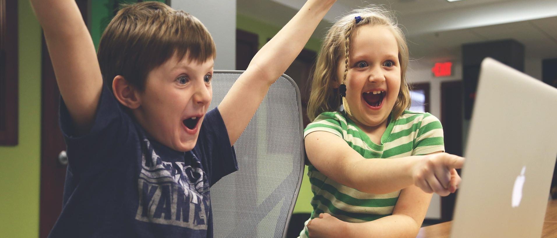 zwei Kinder sitzen an einem Laptop und jubeln