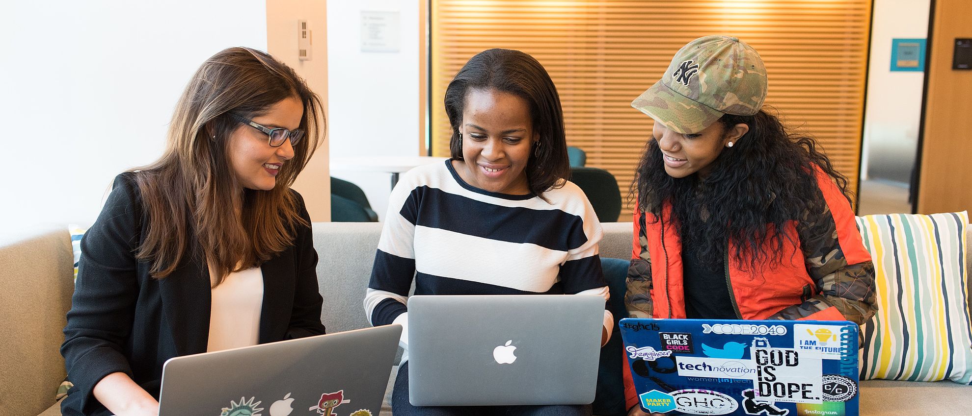 Drei Frauen schauen vergnügt gemeinsam auf einen Laptop in der Mitte und lächeln konzentriert