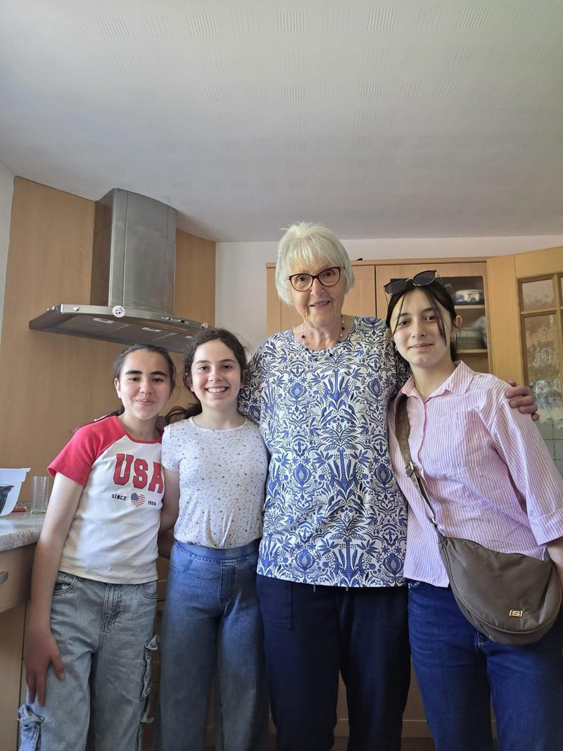 Eine deutsche Seniorin und drei geflüchtete Jugendliche lächeln während eines gemeinsamen Kochtreffens in einer Küche.