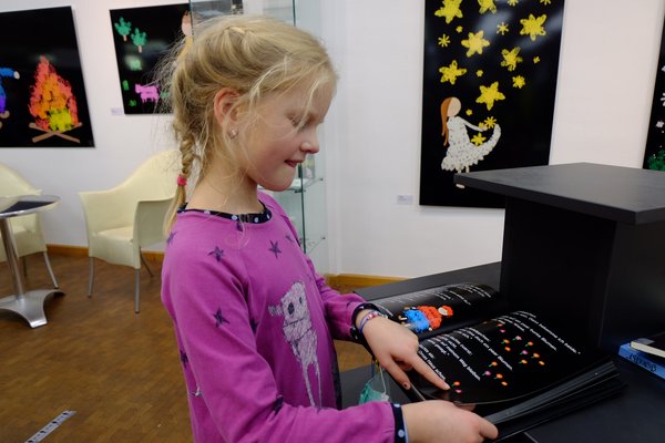 Kind schaut in ein Buch und zeigt mit dem Finger auf eine Seite