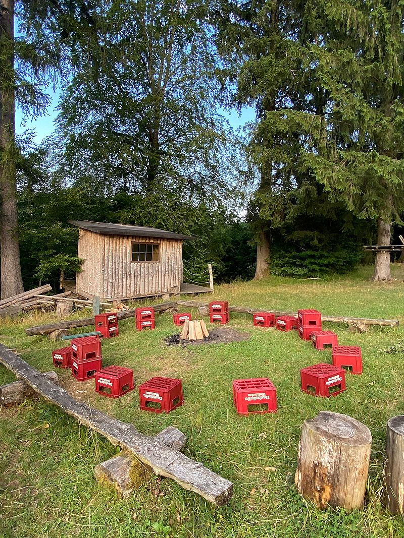 Auf einem Rasen stehen mehrere leere Kisten im Kreis. In der Mitte stehen mehrere Holzstücke.