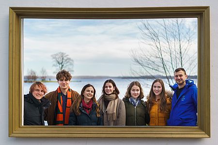Sieben Teammitglieder von EndEndoSilence stehen vor dem Schweriner See hinter einem Bilderrahmen