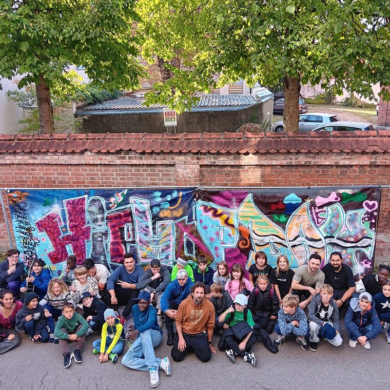 Große Gruppe Jugendlicher sitzt und steht vor einer bunten Graffiti-Wand - Gruppenfoto Hip Hop Day