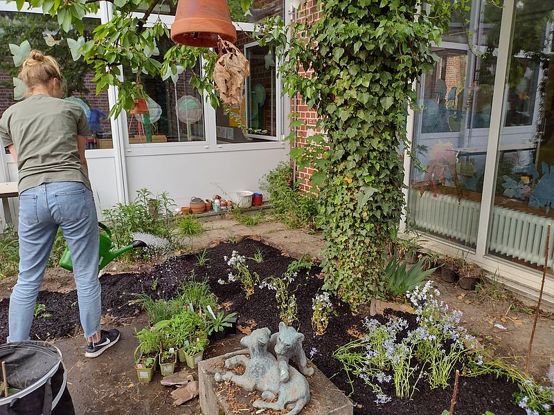 Lehrerin gießt fertig bepflanztes Beet