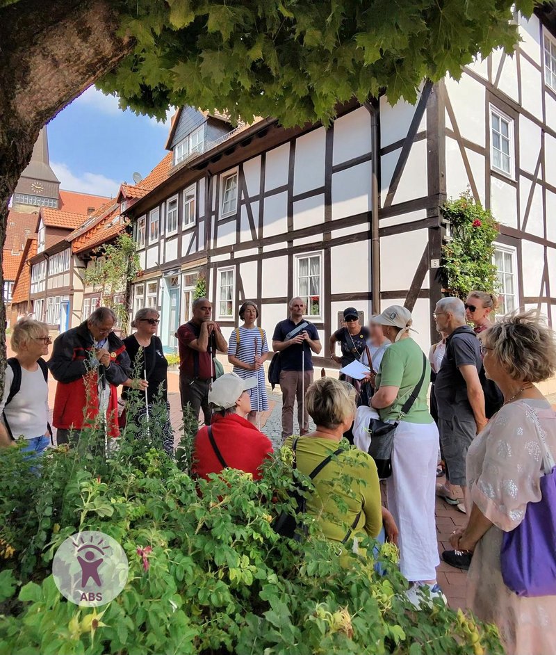 Blinde und sehende Menschen lauschen vor einem Fachwerkhaus