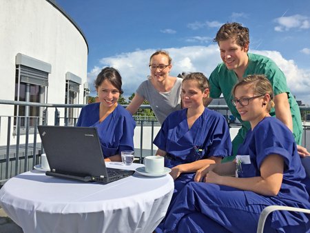 Fünf medizinische Fachpersonen sitzen auf einer Terrasse gemeinsam an einem Laptop und verfolgen eine digitale Fortbildung.