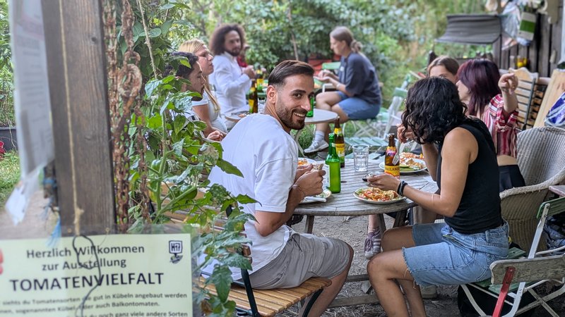 Eine Gruppe von Menschen sitzt in einem Garten gemeinsam an Tischen und isst.