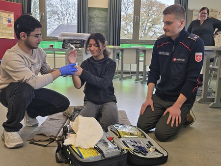 Zwei Schulsanitäter*innen üben gemeinsam mit einem Ausbilder die Wundversorgung am Unterarm