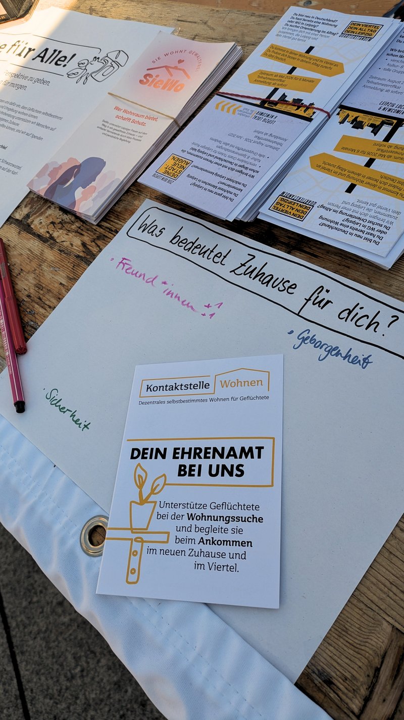 Infoflyer zu ehrenamtlichen Engagement liegen auf einem Tisch. Daneben ein Plakat mit der Frage "Was bedeutet Zuhause für dich". Mit bunten Stiften steht darunter: Freundinnen, Geborgenheit, Sicherheit