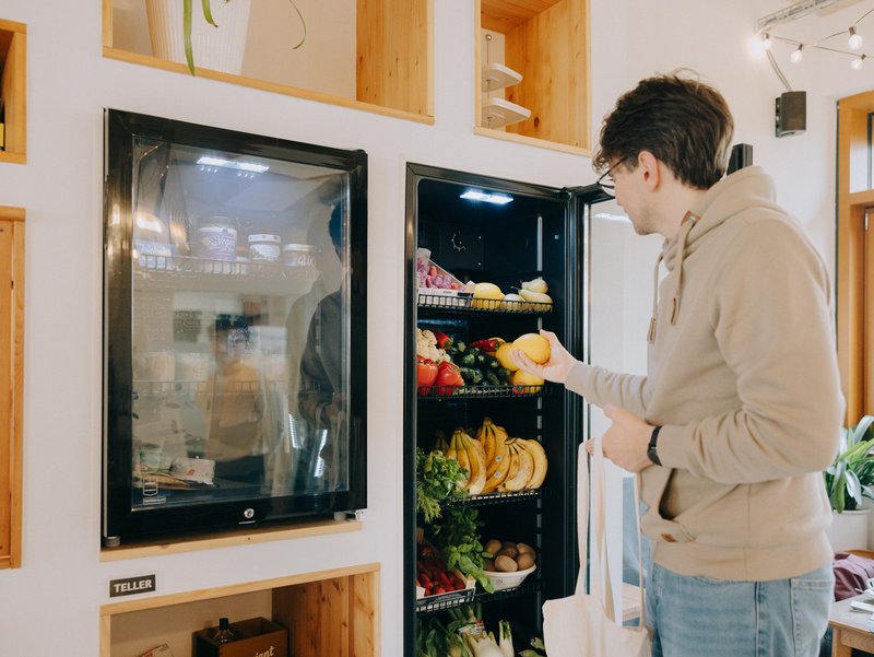Mensch nimmt Obst & Gemüse aus dem Fairteilerkühlschrank