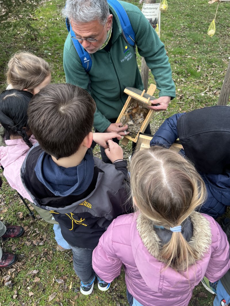 Ein Mann zeigt einen gefüllten Vogelnistkasten. Kinder stehen im Halbkreis vor ihm.