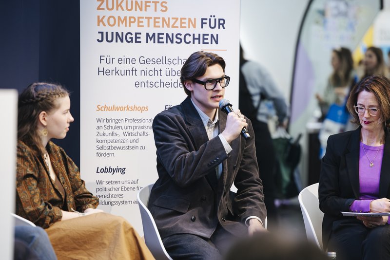 Vorstand Nils hält ein Mikrofon und spricht beim Panel zu Bildungsgerechtigkeit auf der didacta
