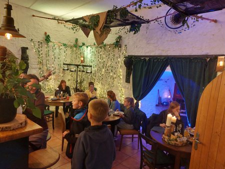 Ein Raum in einem Café mit Tischen und einer Theke. Mehrere Personen sitzen an den Tischen und essen.