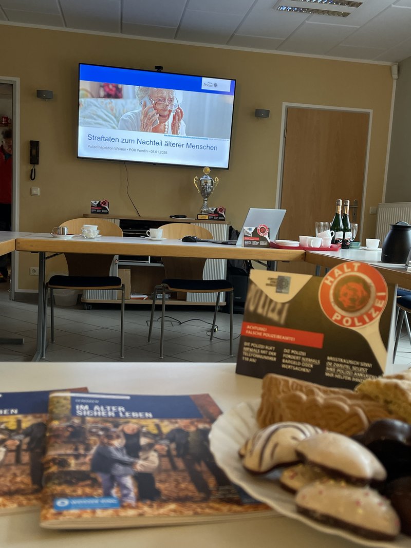 Vordergrund Flyer auf einem Tisch und im Hintergrund ein Bildschirm mit einer Präsentastion