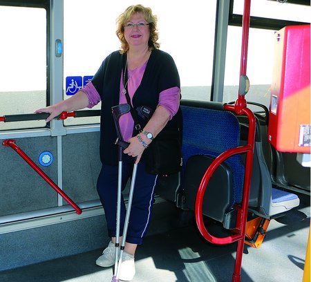 Frau steht im Bus und hält sich mit einer Hand fest. In der anderen Hand hält sie Krücken.