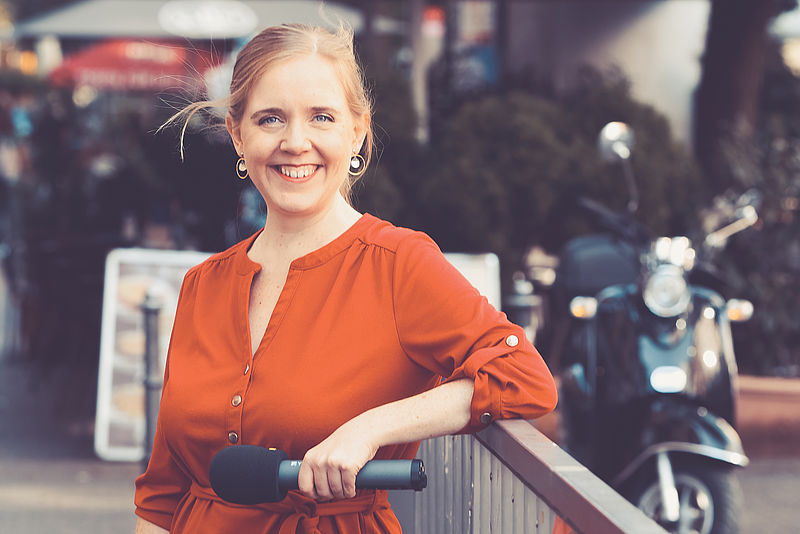 Frau im roten Kleid mit Mikrofon lehnt an Geländer