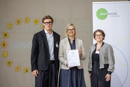 Vorstand Emmelie und Wetzel posieren mit der startsocial Urkunde gemeinsam mit Staatsministerin Schenderlein.