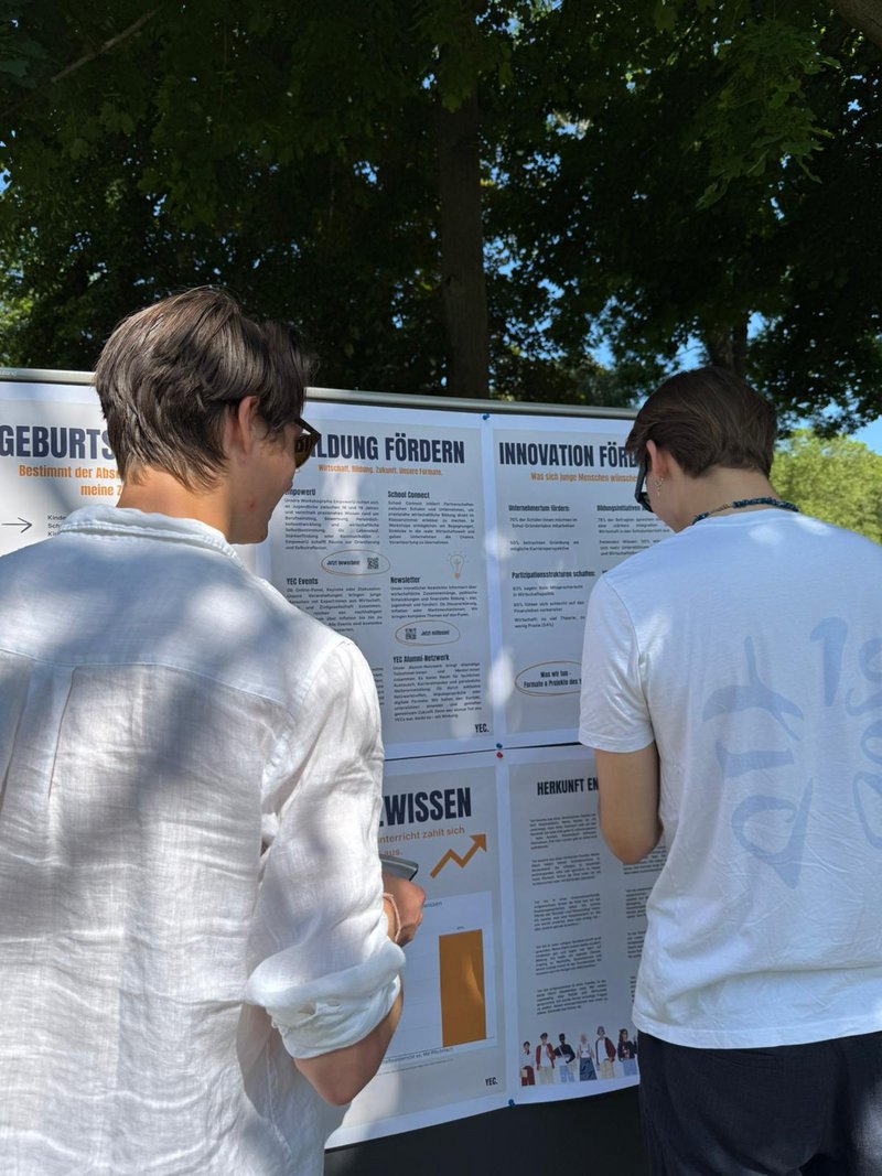 Zwei Ehrenamtliche stehen vor einer Pinnwand mit Infoplakaten zu Bildungsgerechtigkeit.