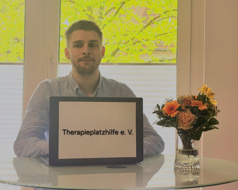 Marvin Petersen sitzt an einem Tisch hinter einem Laptop mit der Aufschrift "Therapieplatzhilfe e. V."