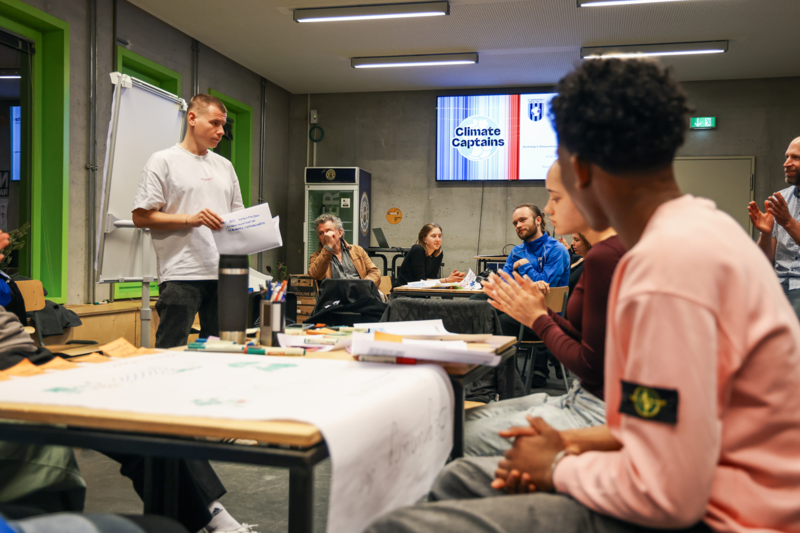 Vier jüngere Personen sitzen um einen Tisch herum und diskutieren die erarbeiteten Materialien, die vor ihnen liegen.