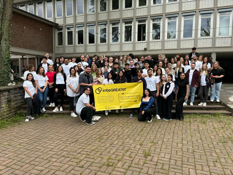 Eine große Gruppe an Mitgliedern und Schülern hält vor der Schule ein Plakat mit dem Vereinsnamen hoch.