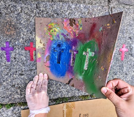 Hände in Gummihandschuhen nehmen nach dem Sprayen eine Schablone mit Kreuzen von der Straße.