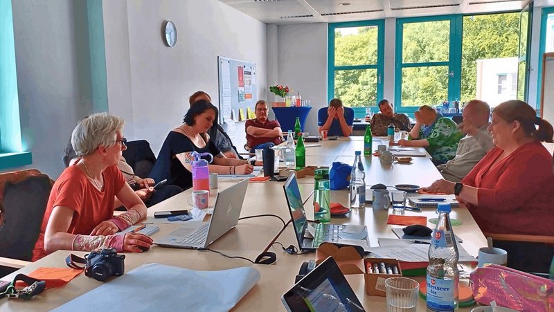 Ein Bild vom Konferenzraum. An dem großen Tisch sitzen 10 Personen der AGH, teilweise mit Notebooks vor sich. Die hintere Person am Kopfende hält sich die Hände vor das Gesicht, weil das Thema sehr anstrengend ist. Gemeinsam erarbeitet die Gruppe die nächsten Schritte der Gremienarbeit
