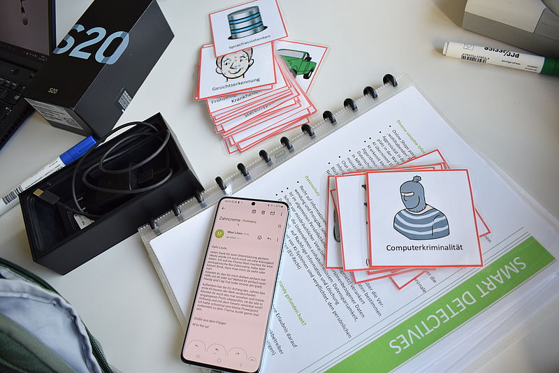 Auf einem Tisch liegen verschiedene Karten mit Bildern, ein Text und ein Handy