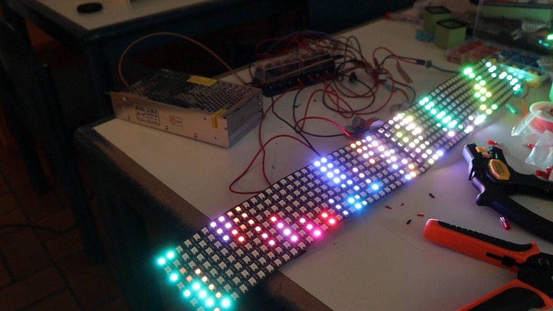 ein unordentlicher Tisch voller Kabel und Werkzeug in der Mitte ist eine LED Matrix die angeschaltet ist 