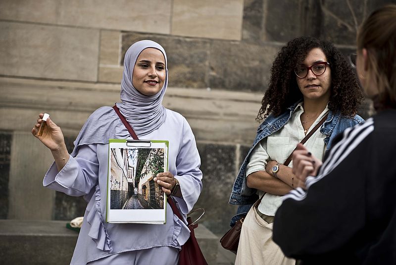 Eine Stadtführerin hält ein Bild aus Damaskus auf der Straße