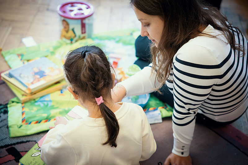 Ein Kind schaut sich ein Buch an mit einer Kinderbeaufsichtigenden.