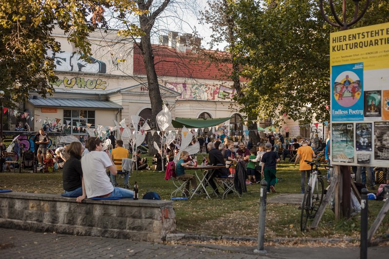 Menschen sitzen auf der Wiese vor dem KulturQuartier Schauspielhaus und lauschen dem Programm