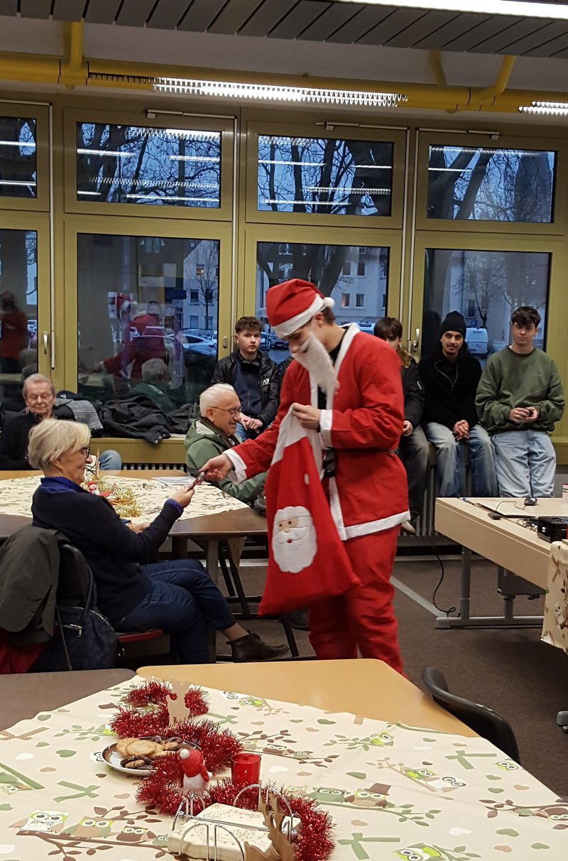 Schüler im Kostüm eines Weihnachtsmannes verteilt kleine Geschenke an Senioren