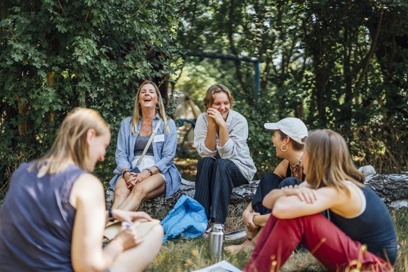 Ehrenamtliche und Teilnehmende sitzen zusammen, lachen und sprechen 