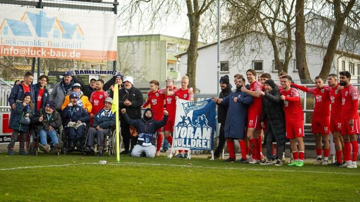 Drei Personen - davon eine mit Rollstuhl - vor einem green-screen. Im Vordergrund Fernsehkameras