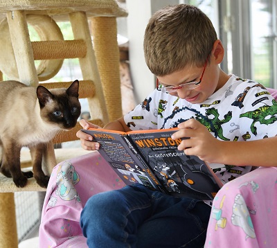 Ein Junge liest einer Katze aus einem Buch vor. 