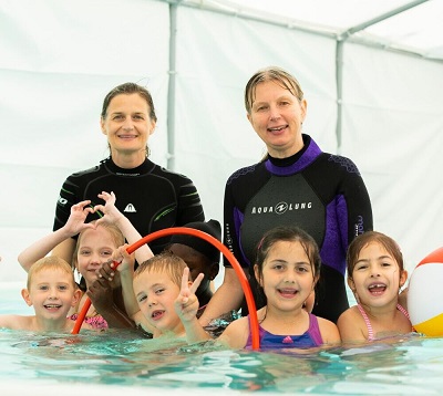 Kinder im Wasser mit zwei Schwimmlehrerinnen  